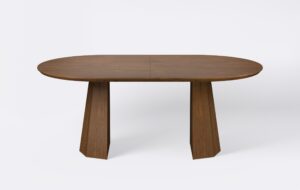 Owalny stół z funkcja rozkładania, na dwóch nogach, fornirowany, o wybarwieniu ciemnego dębu.