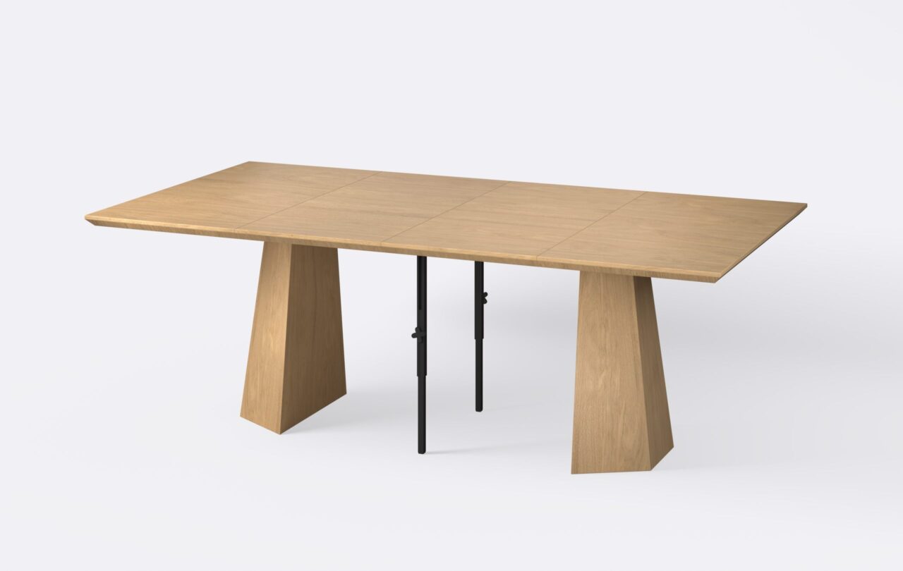 Kwadratowy rozłożony stół z dwoma wkładkami o jasnym wybarwieniu, wykonany z płyty fornirowanej.